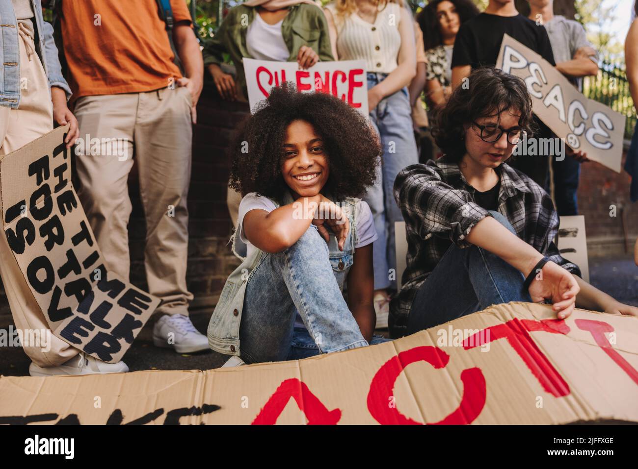 Fröhliches Teenager-Mädchen, das mit einer Gruppe JugendfriedensaktivistInnen an der Kamera lächelt. Multiethnische junge Menschen mit Plakaten und Spruchbändern Stockfoto