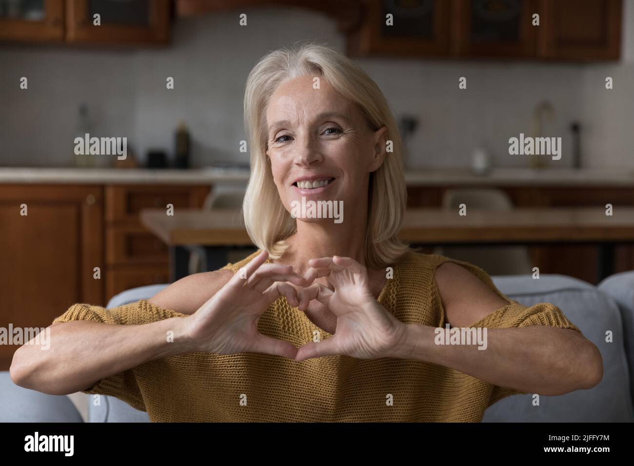 Frau im mittleren Alter von 50s Jahren, die der Kamera ein Herzsymbol zeigt Stockfoto