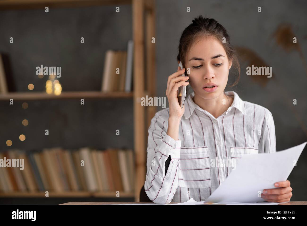 Junge hispanische Frau mit Papieren, die im Heimbüro arbeiten und auf dem Smartphone anrufen, seriöse Geschäftsfrau, die den Brief überprüft und telefoniert, verkauft Telefonsitzend Stockfoto