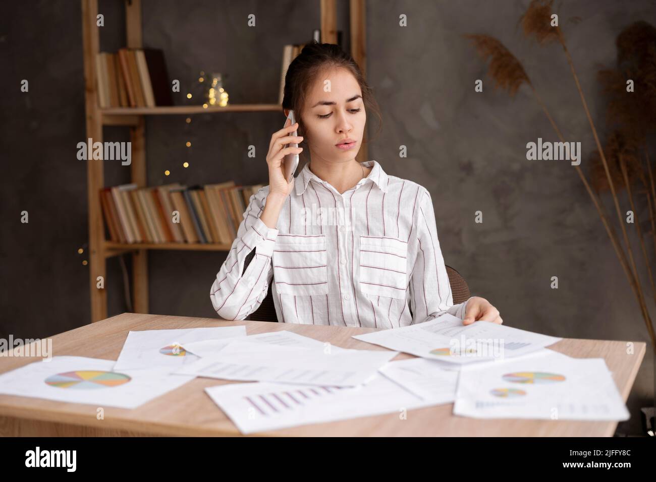 Serious Hispanic junge Geschäftsfrau mit Papieren arbeiten im Home Office und Anrufe auf dem Smartphone. Remote-Job, Technologie und Menschen Stockfoto