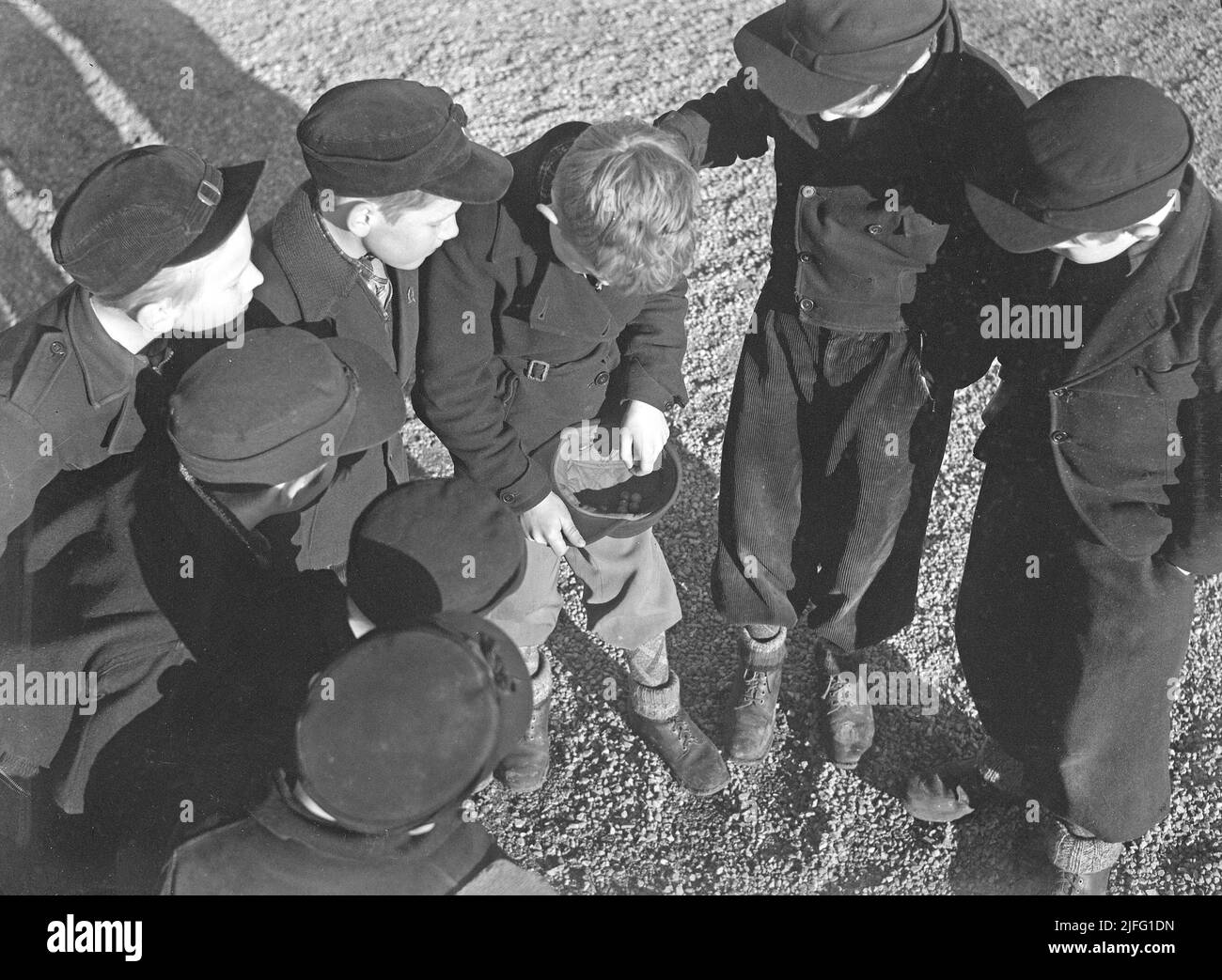 1940s Sommer. Jungs im Freien spielen Murmeln. Ein altmodisches Spiel, bei dem das Ziel ist, die Pyramide aus Murmeln mit nur einem Marmor zu treffen. Wenn du triffst, hast du die Murmeln in der Pyramide gewonnen, sonst ging die Murmel verloren. Es gab auch Varianten des Spiels und verschiedene Arten von Murmeln. Schweden April 1940 Kristoffersson Ref. 111-5 Stockfoto