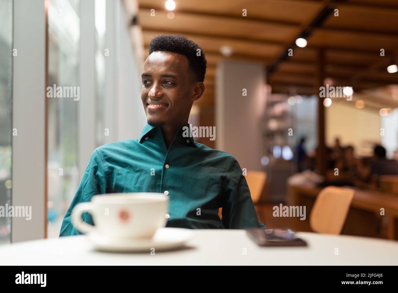 Hübscher junger schwarzer Mann im Café, der durch das Fenster schaut Stockfoto