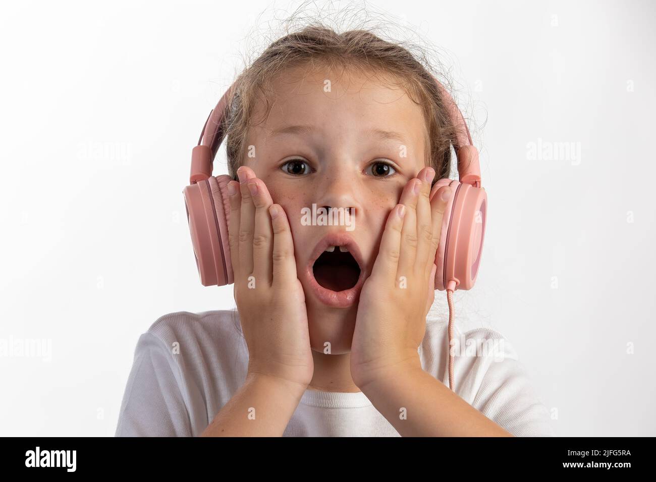 Nahaufnahme eines jungen Mädchens mit rosa Kopfhörern, das Musik hört und überrascht ist, während es direkt in die Kamera schaut Stockfoto