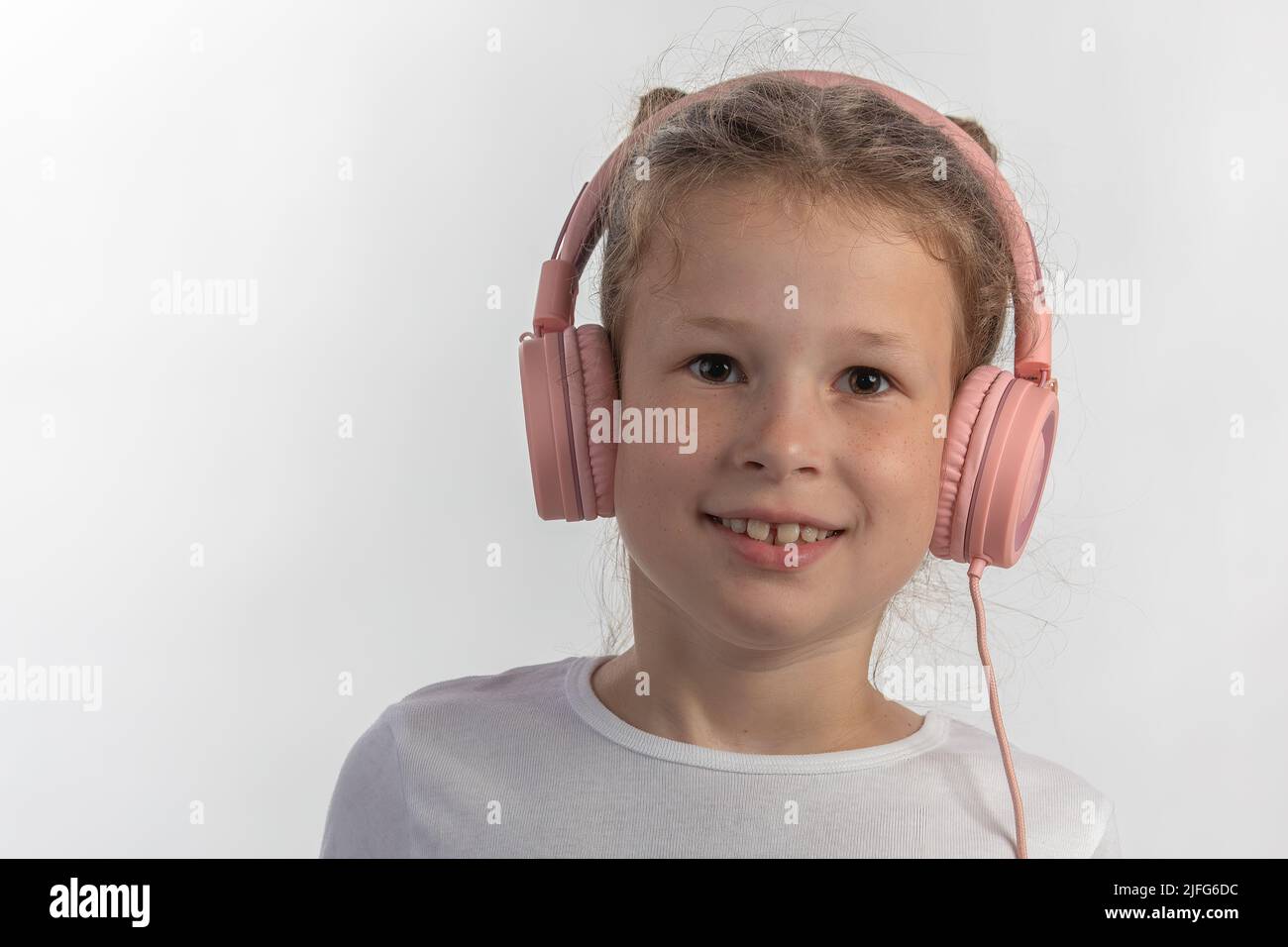 Nahaufnahme eines jungen Mädchens mit rosa Kopfhörern, das Musik hört und direkt in die Kamera schaut Stockfoto