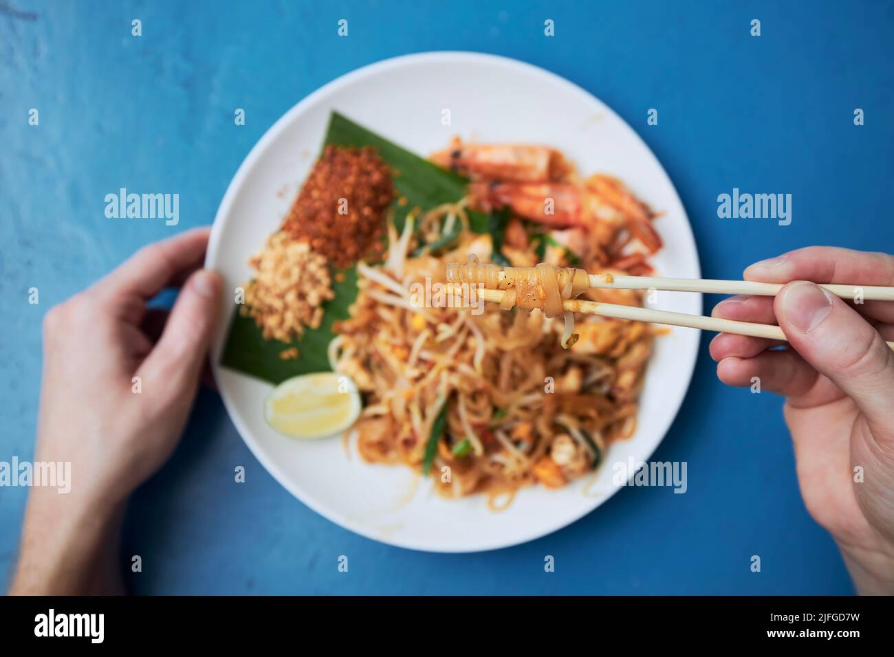 Essstäbchen mit der Hand über dem Teller halten. Mann isst Pad Thai-Essen im Straßenrestaurant. Stockfoto