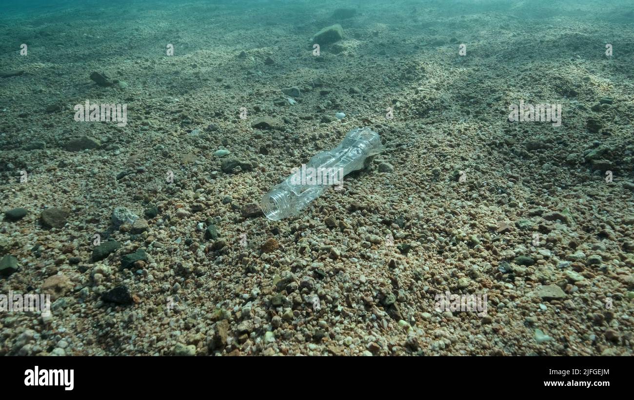 Aus der Nähe liegt eine Plastikflasche in den Sonnenstrahlen auf dem Meeresboden, im Küstenbereich am Strand. Plastikverschmutzung des Ozeans. Rotes Meer, Ägypten Stockfoto
