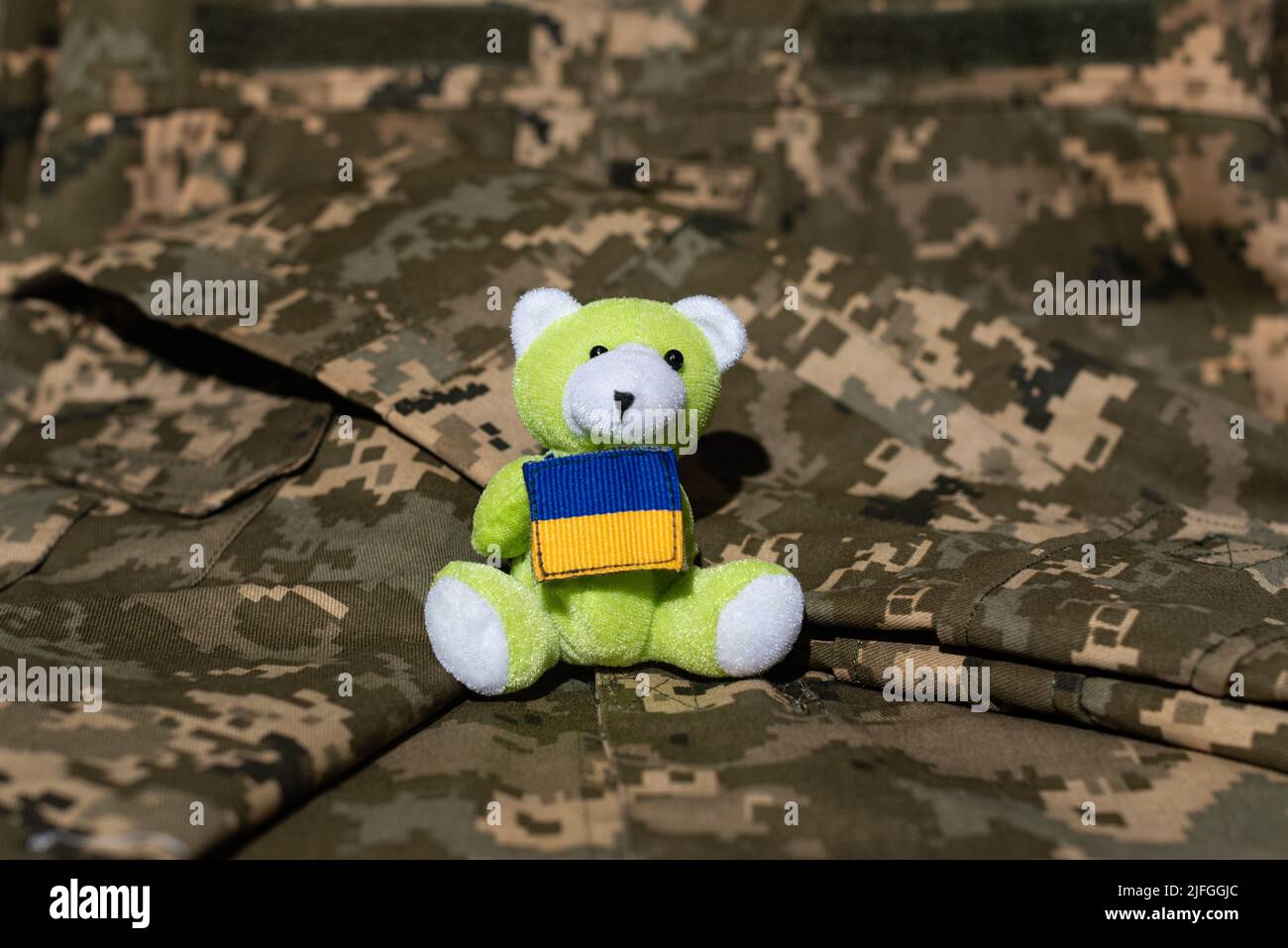 Teddybär hält die Flagge der Ukraine vor dem Hintergrund einer Militäruniform Stockfoto