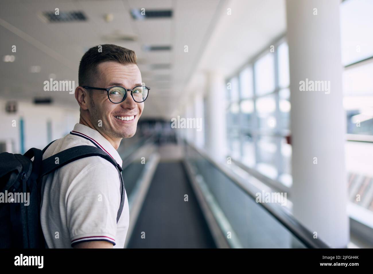 Porträt eines lächelnden Reisenden am Flughafen. Glücklicher Mann, der vor seiner Reise mit dem Flugzeug die Kamera ansah. Stockfoto