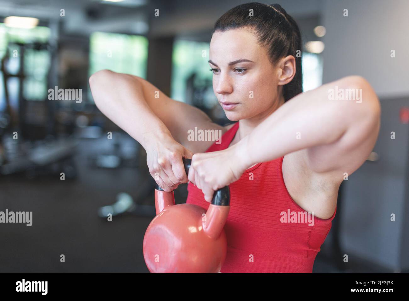 Junge kaukasische Frau, die im Fitnessstudio mit Kettlebell trainiert Stockfoto