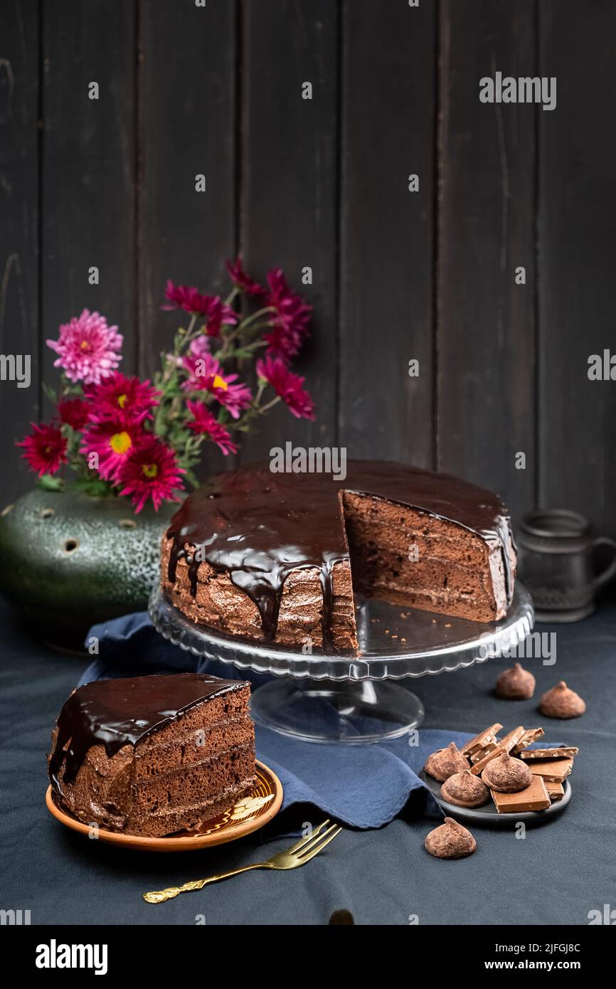 Eine Portion köstlicher hausgemachter dunkler Schokoladenkuchen Dessert mit Ganache-Glasur auf dem Kuchenständer über dunklem rustikalem Holzhintergrund Stockfoto