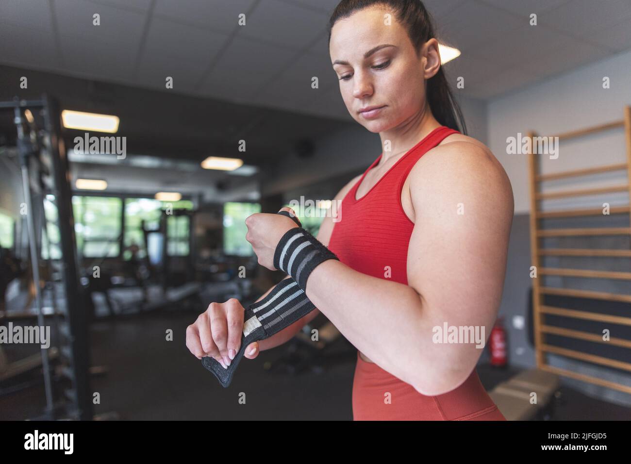 Junge kaukasische Frau, die im Fitnessstudio die Handgelenkumwicklung anpasst Stockfoto