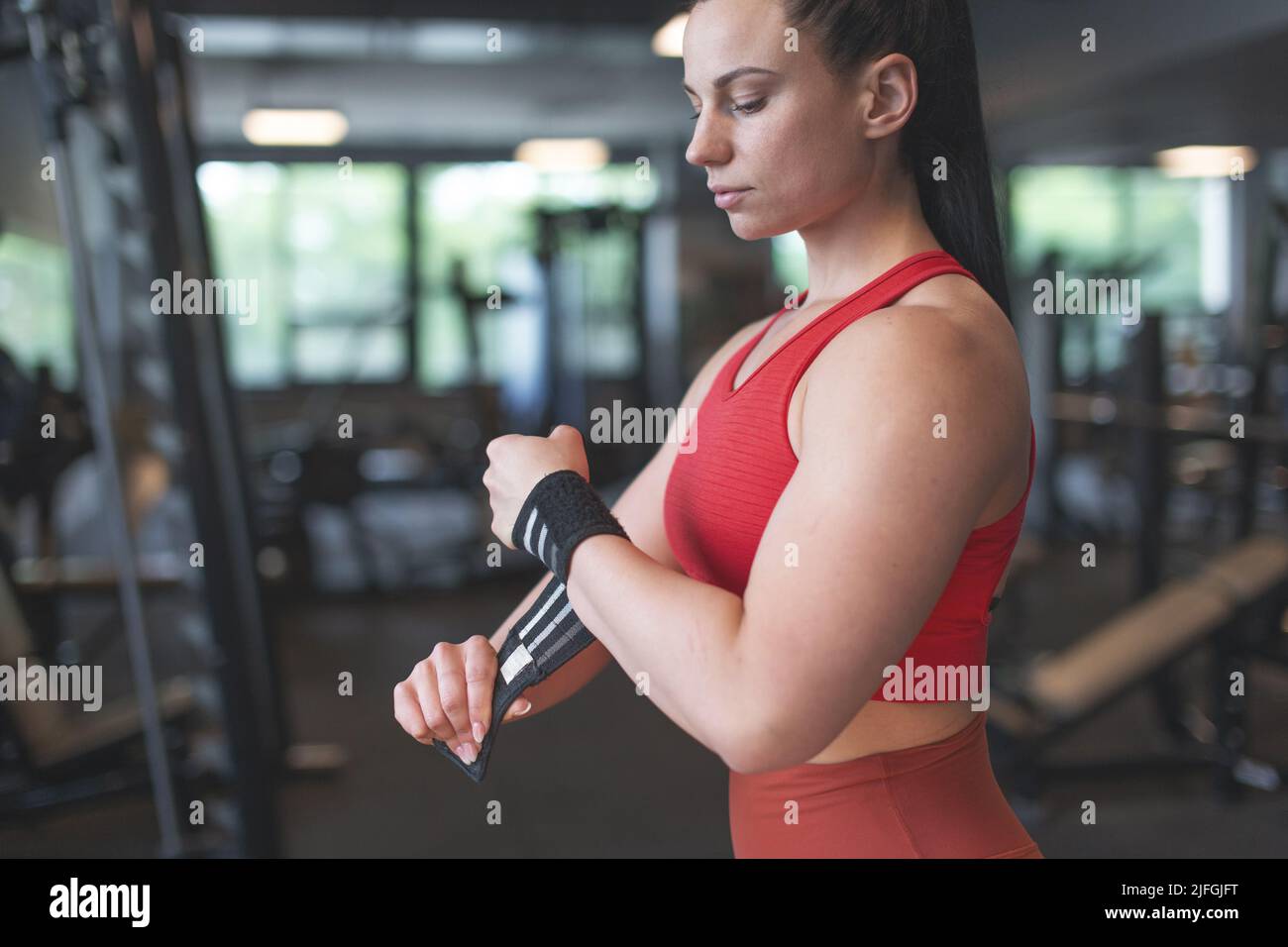 Junge kaukasische Frau, die das Handgelenk in der Profilansicht des Fitnessstudios anpasst Stockfoto