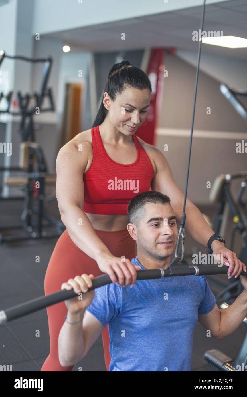 Junge motivierte kaukasische Personal Trainer hilft dem Kunden auf dem Fitness-Studio-Station Stockfoto