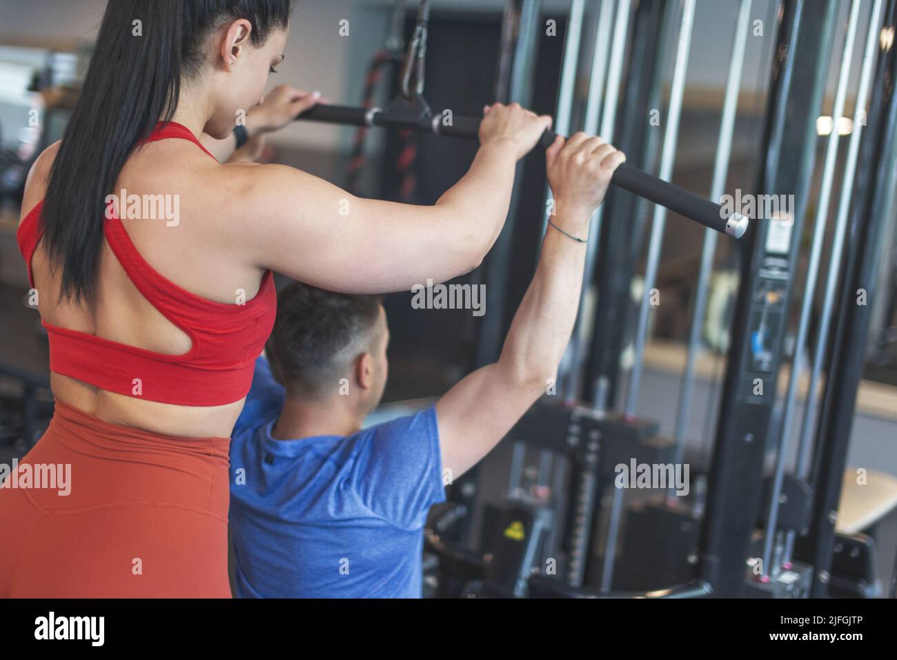 Der junge Personal Trainer hilft dem Kunden auf der Fitnessstation beim Training, Rückansicht Stockfoto