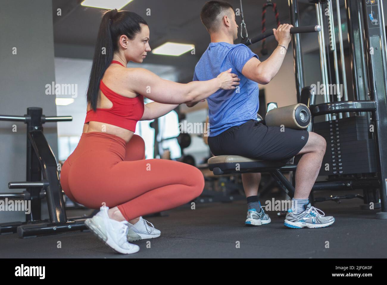 Junge kaukasische Personal Trainer Frau hilft Client auf Gym Station Anpassung zurück Stockfoto