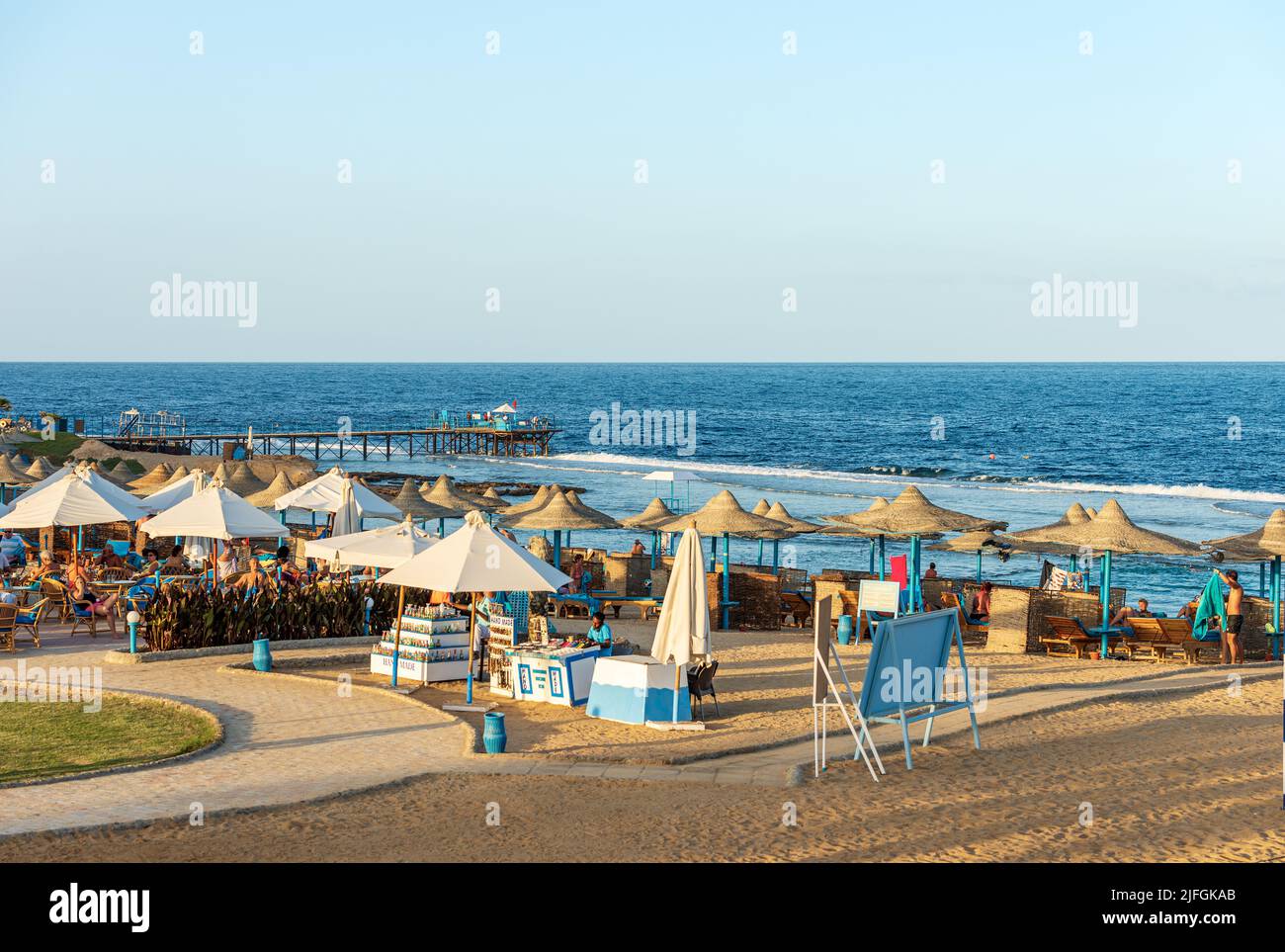 Rotes Meer in der Nähe von Marsa Alam, Sandstrand mit Strohschirmen, Liegestühlen und vielen Touristen, Pier über dem Riff zum Tauchen, Schnorcheln und Schwimmen. Stockfoto