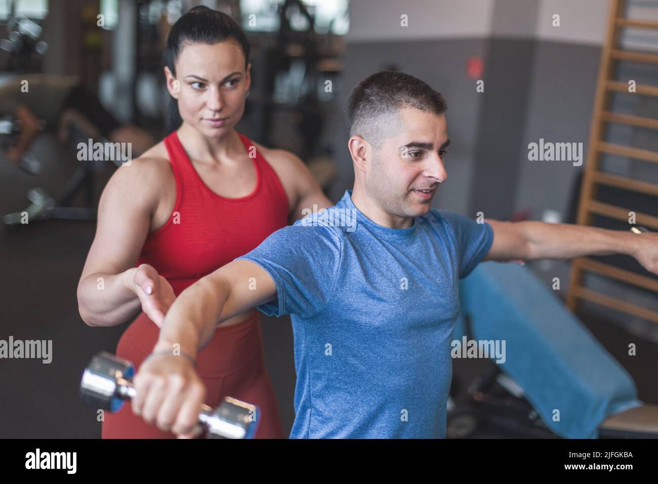 Junge sportliche kaukasische Personal Trainer Frau hält Kunden Ellbogen während des Trainings mit Hanteln Stockfoto