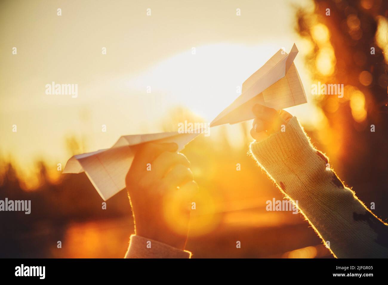Zwei Papierflugzeuge in Händen, die sich bei Sonnenuntergang anguten. Junge Menschen halten Papierflugzeuge, Liebe, Beziehungen Konzept. Stockfoto