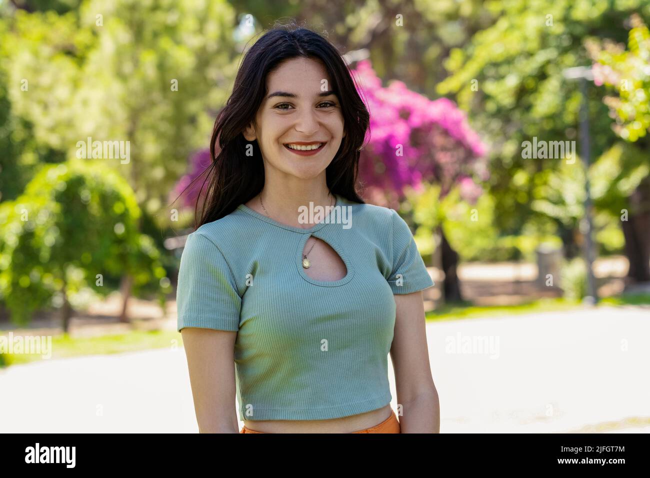 Junge Brünette Mädchen lächelnd glücklich tragen türkisfarbenen T-Shirt auf Stadtpark stehen, im Freien Blick auf die Kamera während posiert. Natürliches Schönheitskonzept. Be Stockfoto