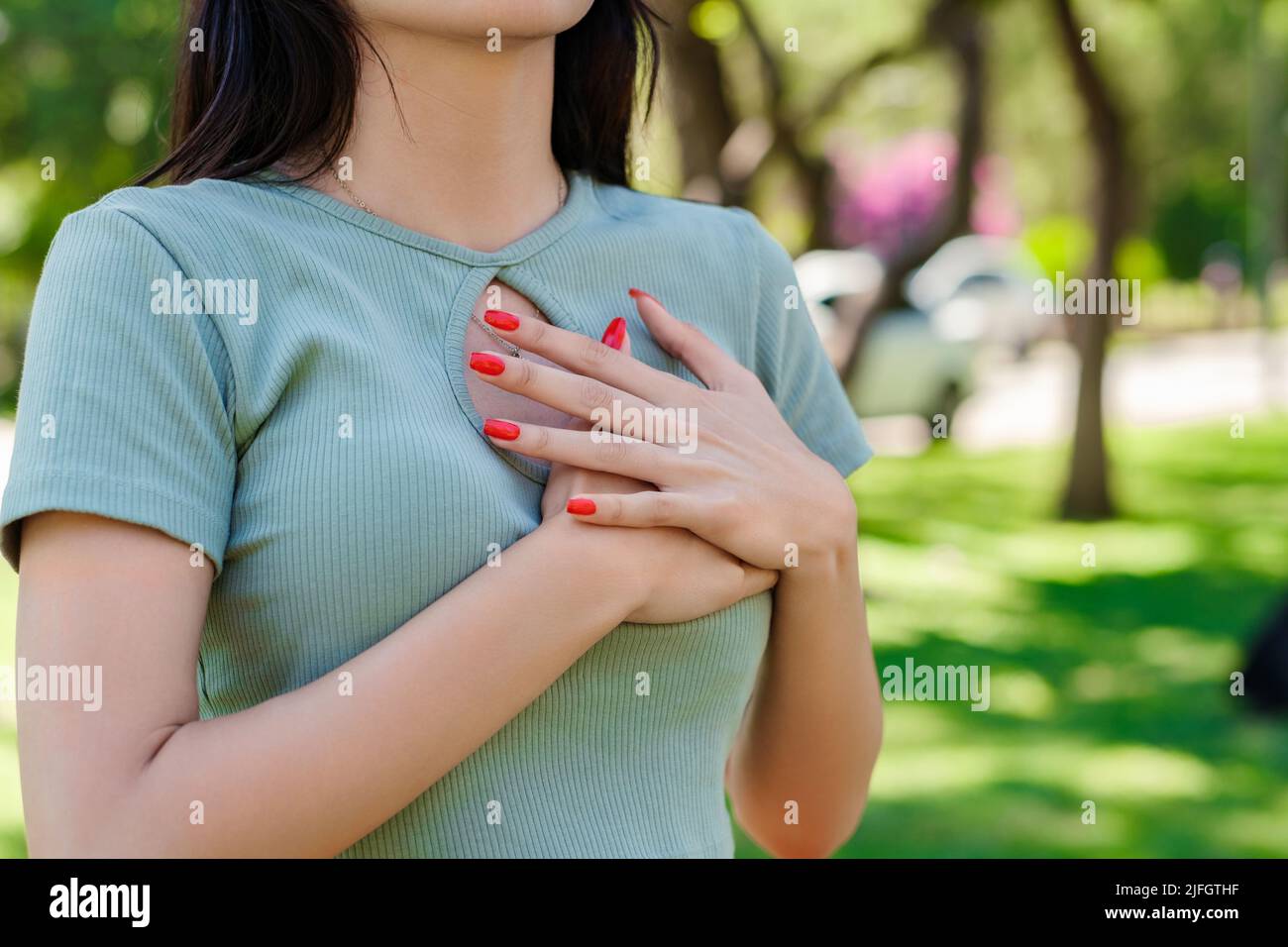 Auf Die Brust Gefallen Frau Die junge kaukasische Frau, die T-Shirt trägt, steht im Stadtpark