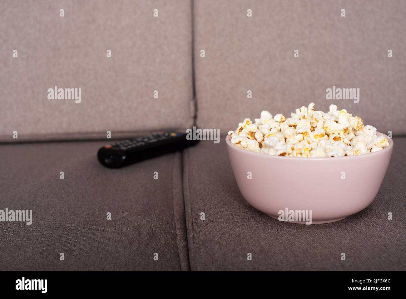 Schüssel mit Popcorn und tv-Fernbedienung auf dem Sofa Stockfoto
