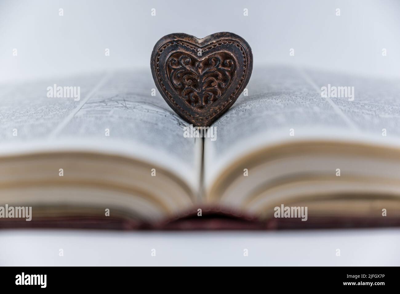 Herzförmige Holzfigur. Großes offenes Buch. Enzyklopädie in rotem Hardcover. Braunes Amulett mit Holzschnitzerei. Nahaufnahme. Selektiver Fokus. Stockfoto