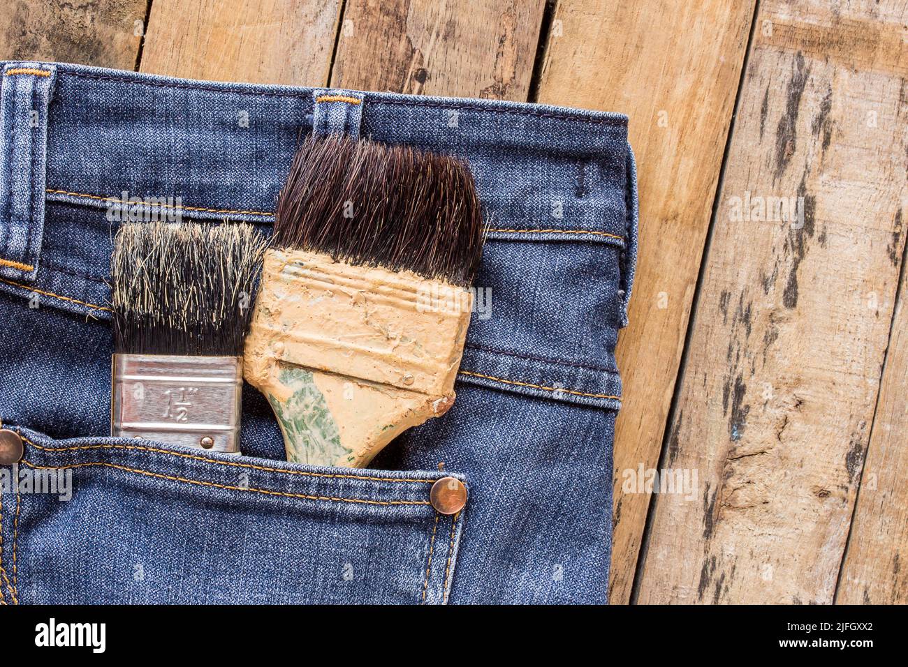 Zwei Farbpinsel in Jeans-Tasche auf Holztisch Stockfoto
