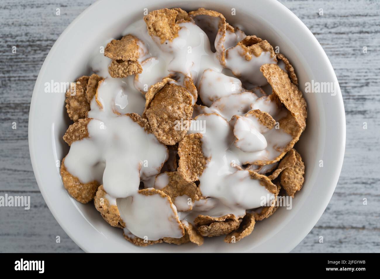 Vollkorn glasierte Flocken mit Joghurt auf dem Teller, Nahaufnahme, Draufsicht. Gesundes Frühstück, Vollkornmüsli in einer Schüssel Stockfoto