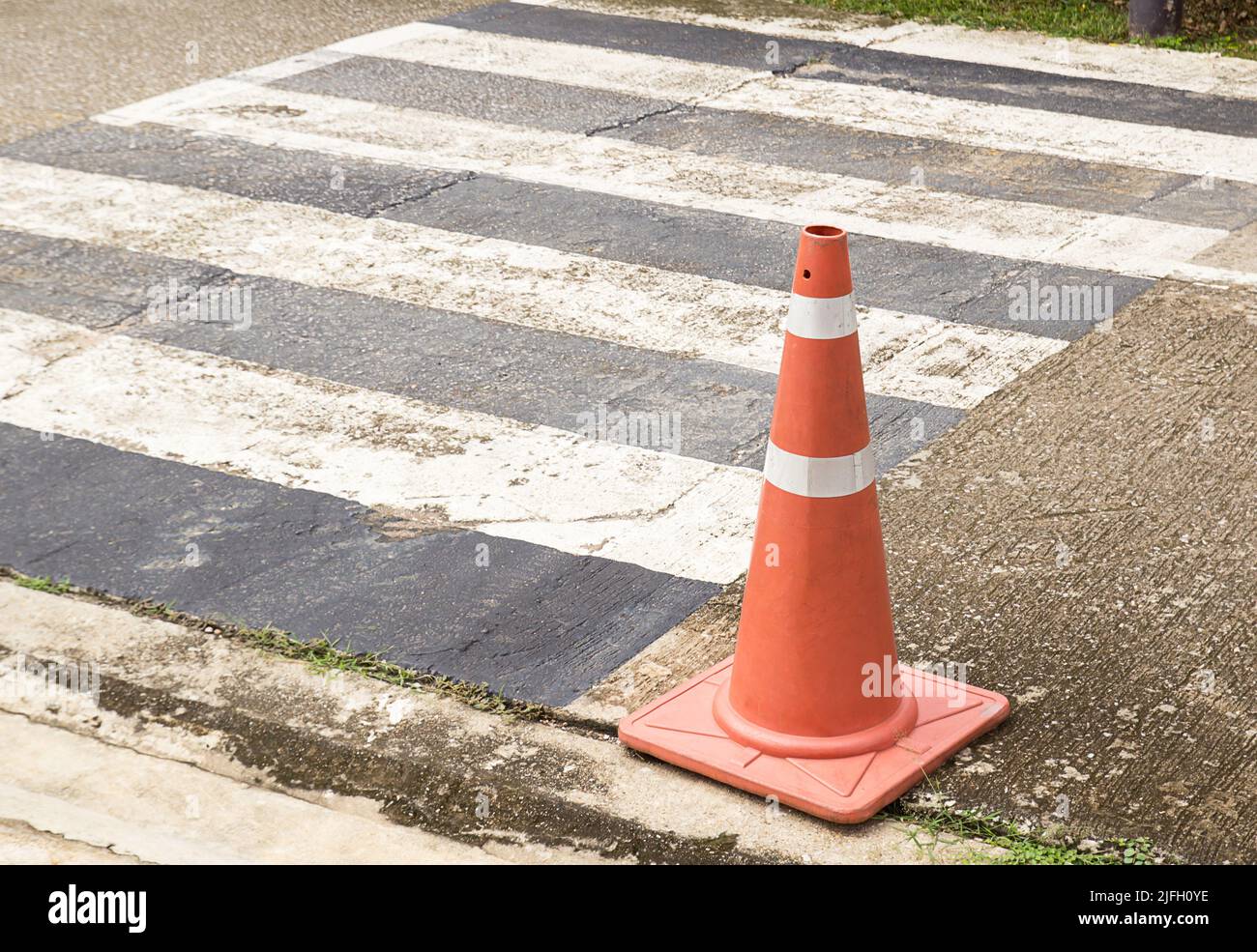 Nahaufnahme leuchtend orange Verkehrskegel stehen in einer Reihe auf Asphalt. Beton Bürgersteig mit gelb rot und weiß Verkehrsschild. Stockfoto