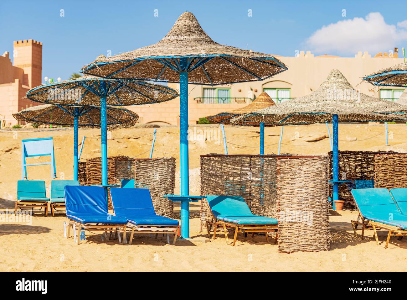 Sandstrand am Roten Meer mit einer Gruppe von Strohschirmen und Liegestühlen in der Nähe von Marsa Alam, Ägypten, Afrika. Stockfoto