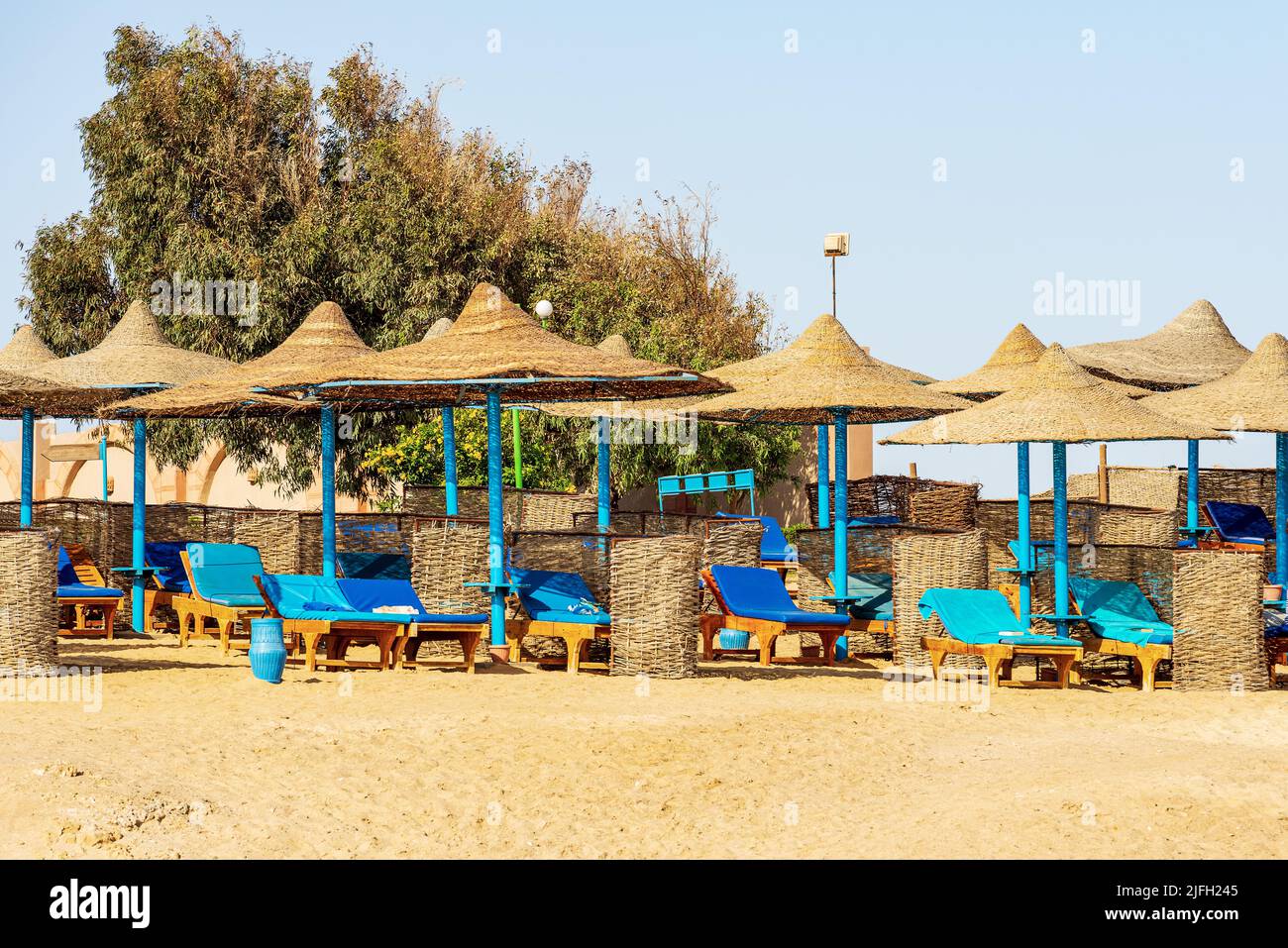 Sandstrand am Roten Meer mit einer Gruppe von Strohschirmen und Liegestühlen in der Nähe von Marsa Alam, Ägypten, Afrika. Stockfoto