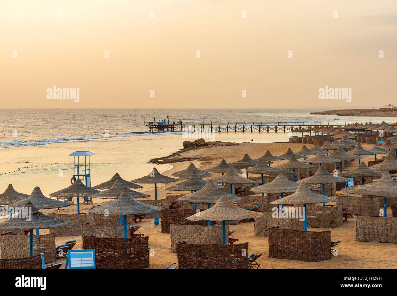 Sandstrand in der Nähe von Marsa Alam mit einem Pier über dem Korallenriff zum Tauchen, Schnorcheln und Schwimmen und einer Gruppe von Sonnenschirmen. Ägypten, Afrika. Stockfoto