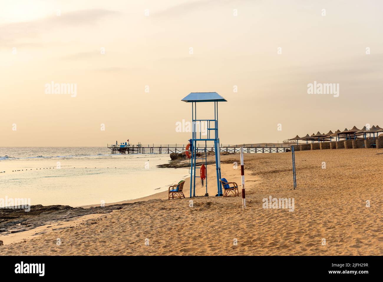 Sandstrand in der Nähe von Marsa Alam mit einem Pier über dem Korallenriff zum Tauchen, Schnorcheln und Schwimmen und einer Gruppe von Sonnenschirmen. Ägypten, Afrika. Stockfoto