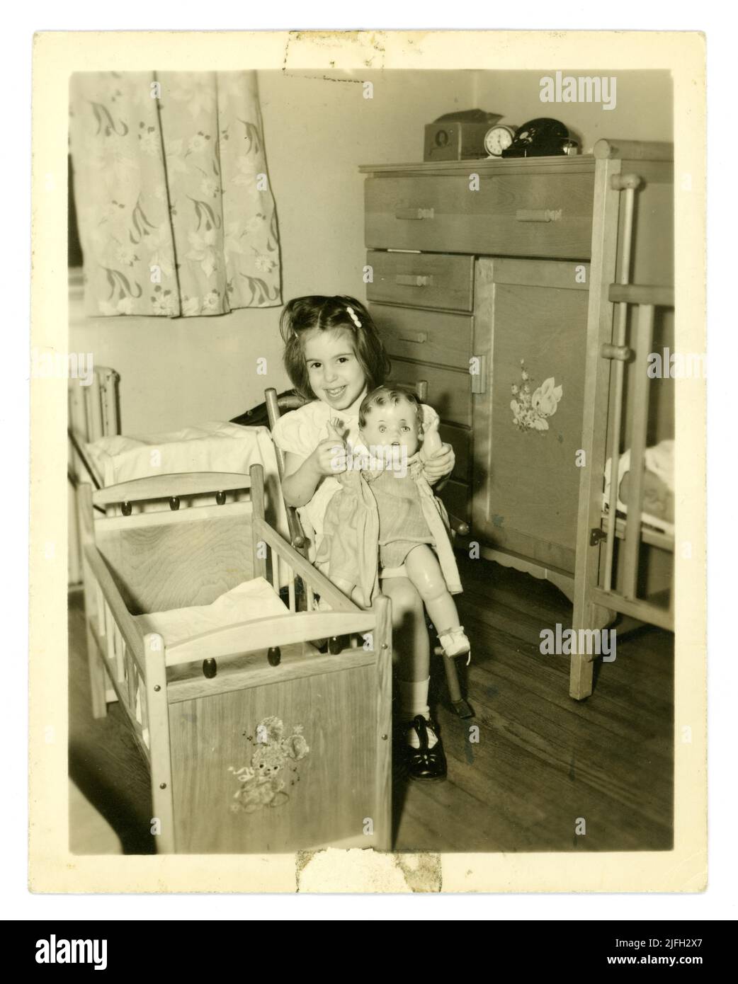 Originalaufnahme aus den 50er Jahren eines niedlichen, glücklichen jungen Mädchens im Alter von etwa 4 oder 5 Jahren, das mit einer Puppe in ihrem Schlafzimmer zu Hause spielt. Möbel für Schlafzimmer aus der Mitte des Jahrhunderts. GROSSBRITANNIEN Stockfoto
