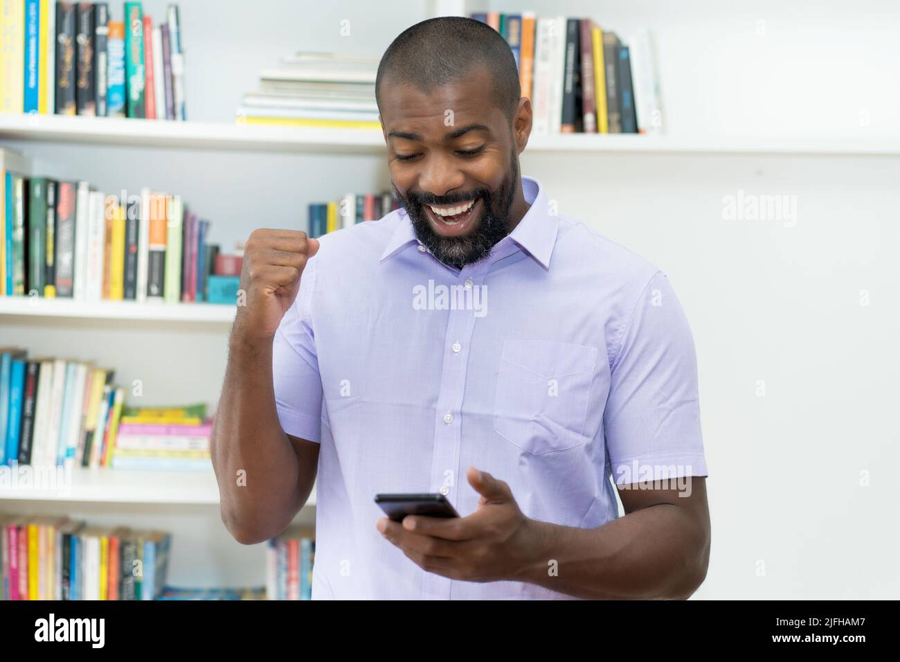 afroamerikanischer reifer erwachsener Geschäftsmann erhält am Telefon im Büro eine Nachricht mit guten Nachrichten Stockfoto