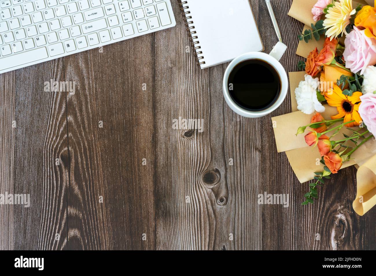Schreibtisch mit Computertastatur, gemischtem Blumenstrauß und einer Tasse Kaffee auf Holzhintergrund Stockfoto