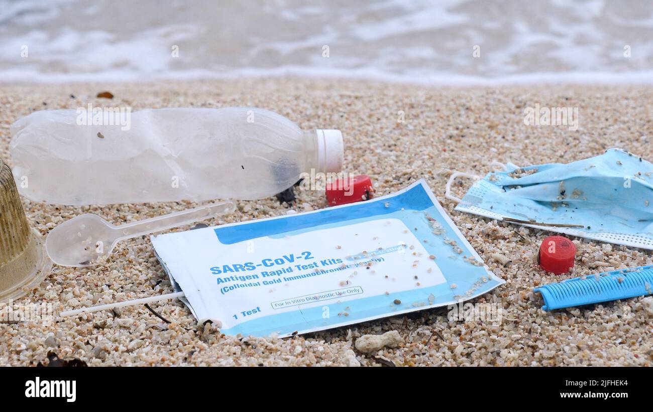 Abfall während COVID-19. Medizinische Gesichtsmasken und Covid-Test am Strand mit Wellen auf dem Hintergrund verwendet. Verschmutzung durch Ozeanplastik Stockfoto