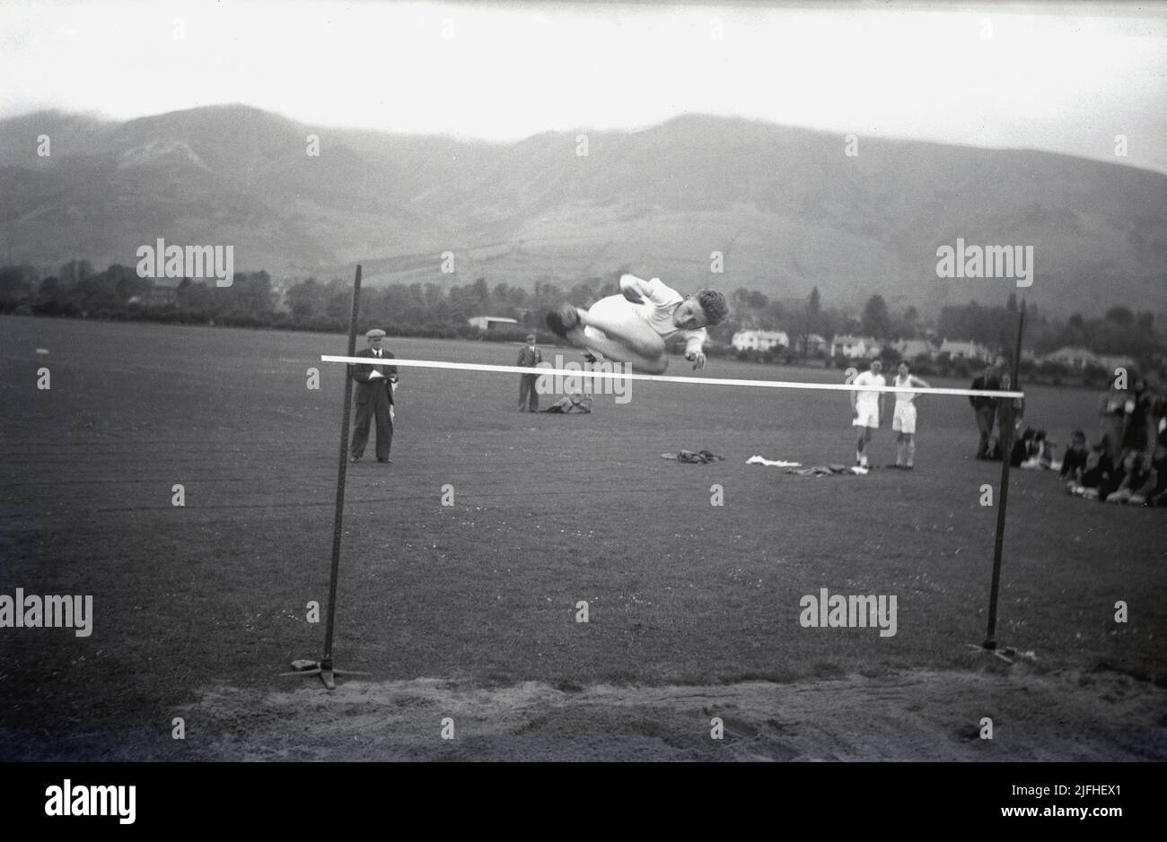 1954, historisch, draußen auf einem Sportplatz, ein Junge, der den Hochsprung macht und zuerst mit einem Sandkasten unter der Stange über die Füße springt, Schottland, Großbritannien. Stockfoto