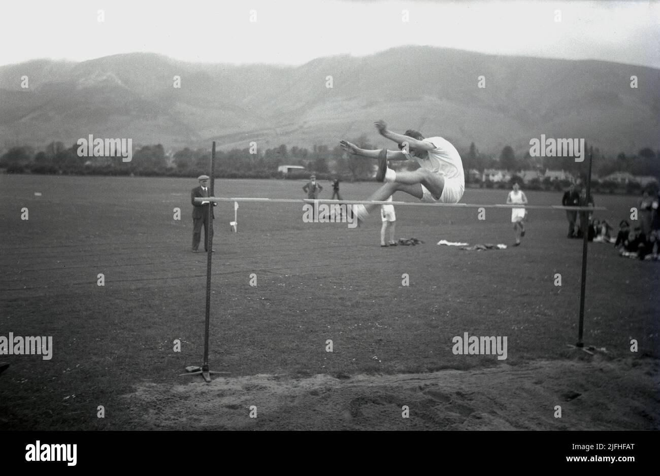 1952, historisch, draußen auf einem Grasfeld, mit Hochlandbergen in der Ferne, ein älterer männlicher Student in der Luft, der den Hochsprung macht, Schottland, Großbritannien. Stockfoto