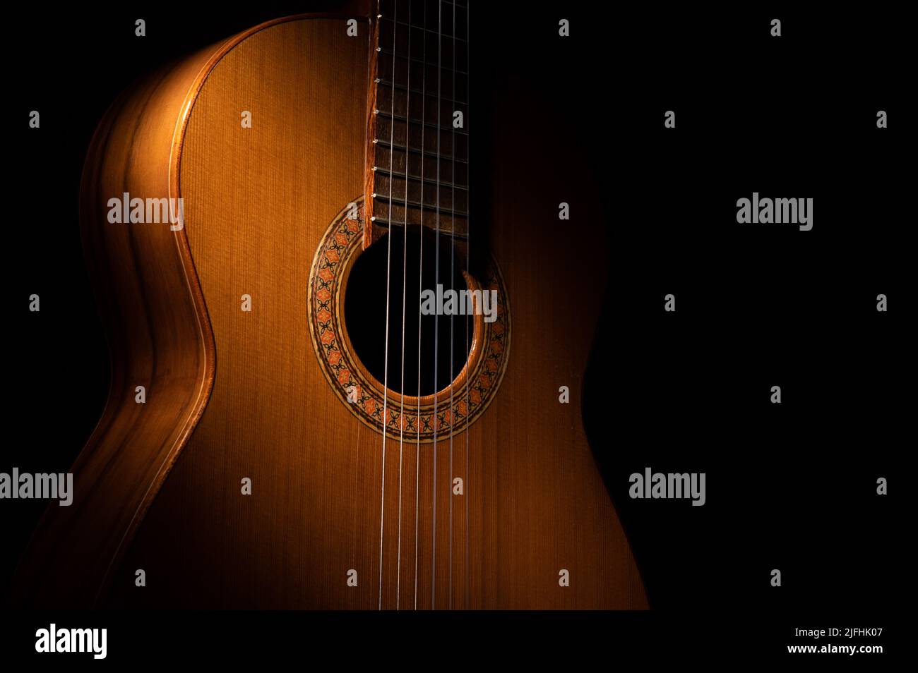 Spanische klassische Gitarre aus der Nähe, dramatisch beleuchtet auf einem schwarzen Hintergrund mit Kopierraum. Stockfoto