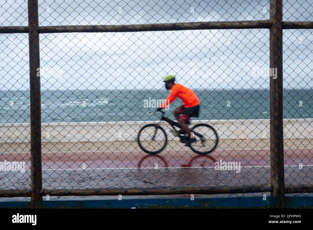 Silhouetten von Radfahrern, die bei Regen hinter dem Sportzaun vorbeifahren. Salvador, Bahia, Brasilien. Stockfoto