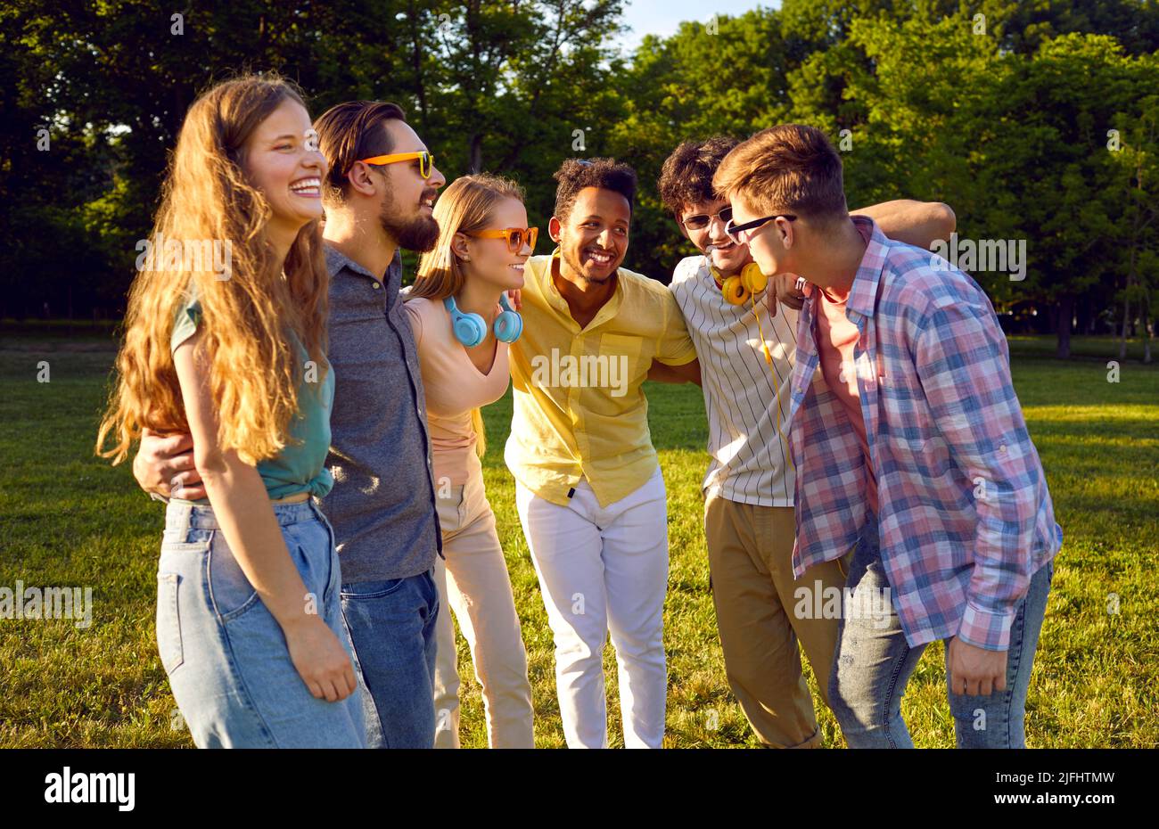 Fröhliche und laute Gesellschaft der jungen Freunde, die sich im Sommer gemeinsam entspannen, im grünen Park. Stockfoto