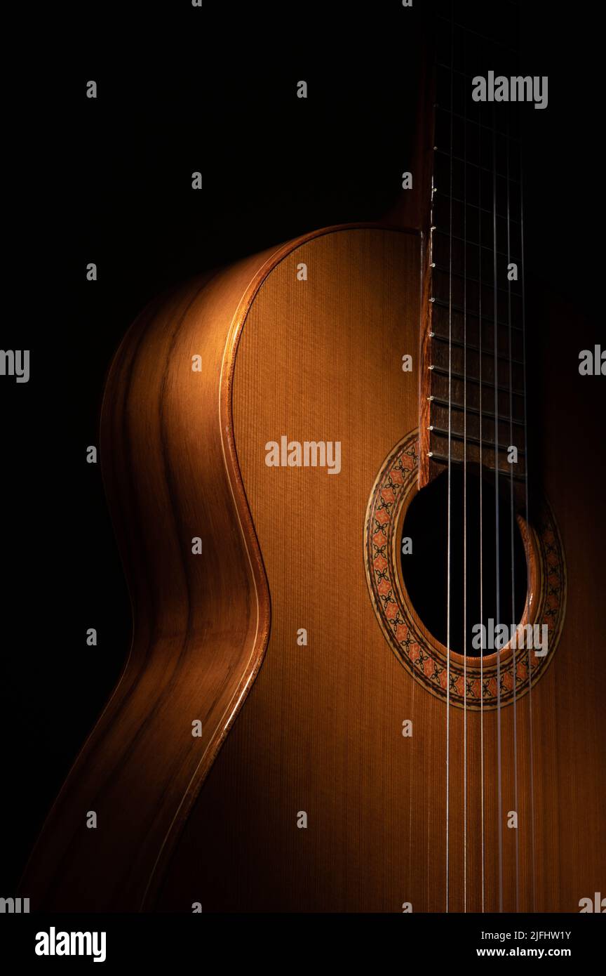 Spanische klassische Gitarre und Hände des Gitarristen aus nächster Nähe auf schwarzem Hintergrund mit Kopierraum und dramatischer Beleuchtung Stockfoto