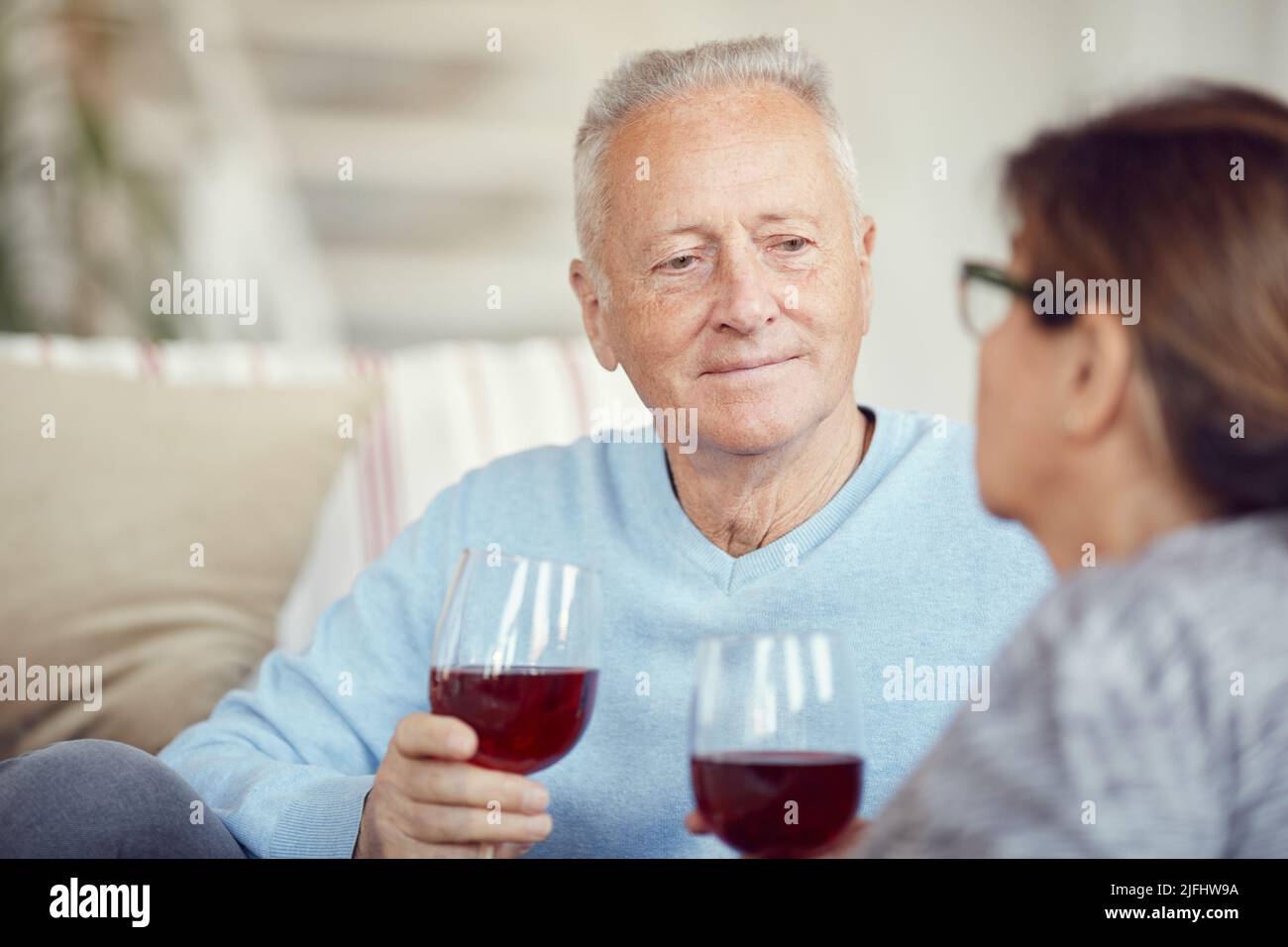 Inhalt hübscher älterer Mann mit Weinglas, der seiner Frau zuhört, während er romantische Zeit mit einer geliebten Person genießt Stockfoto