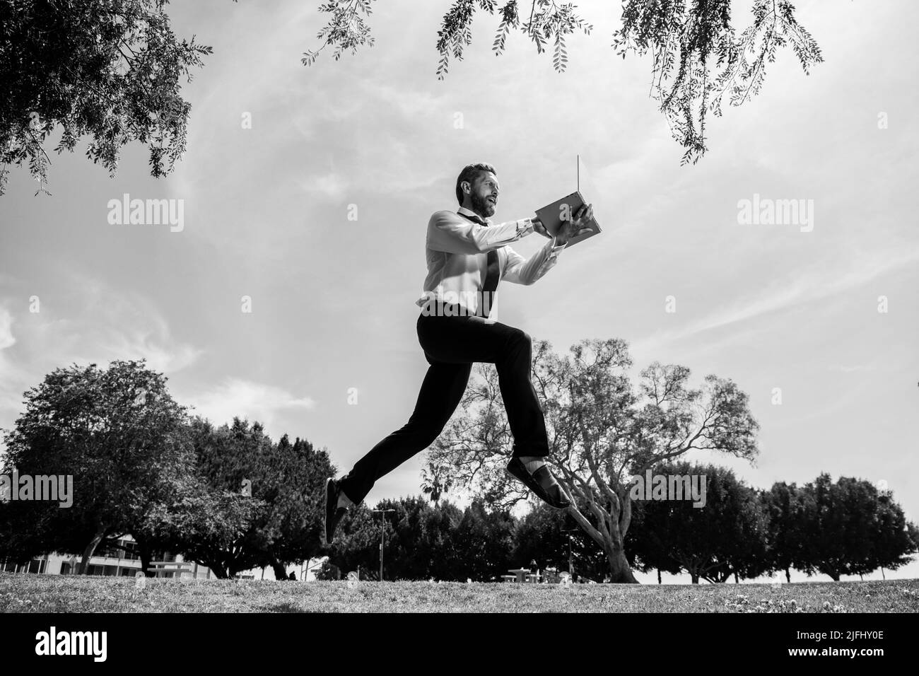 Springender Geschäftsmann mit Laptop im Park. Konzept der schnellen Internet mit laufenden Geschäftsmann mit einem Laptop Stockfoto