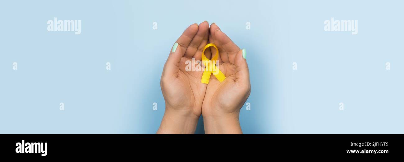 Gelbes Goldband in den Händen eines Mädchens auf blauem Hintergrund. Kinderkrebskonzept. Monat der Sensibilisierung. Kinderkrebstag Februar 15. Internet Stockfoto