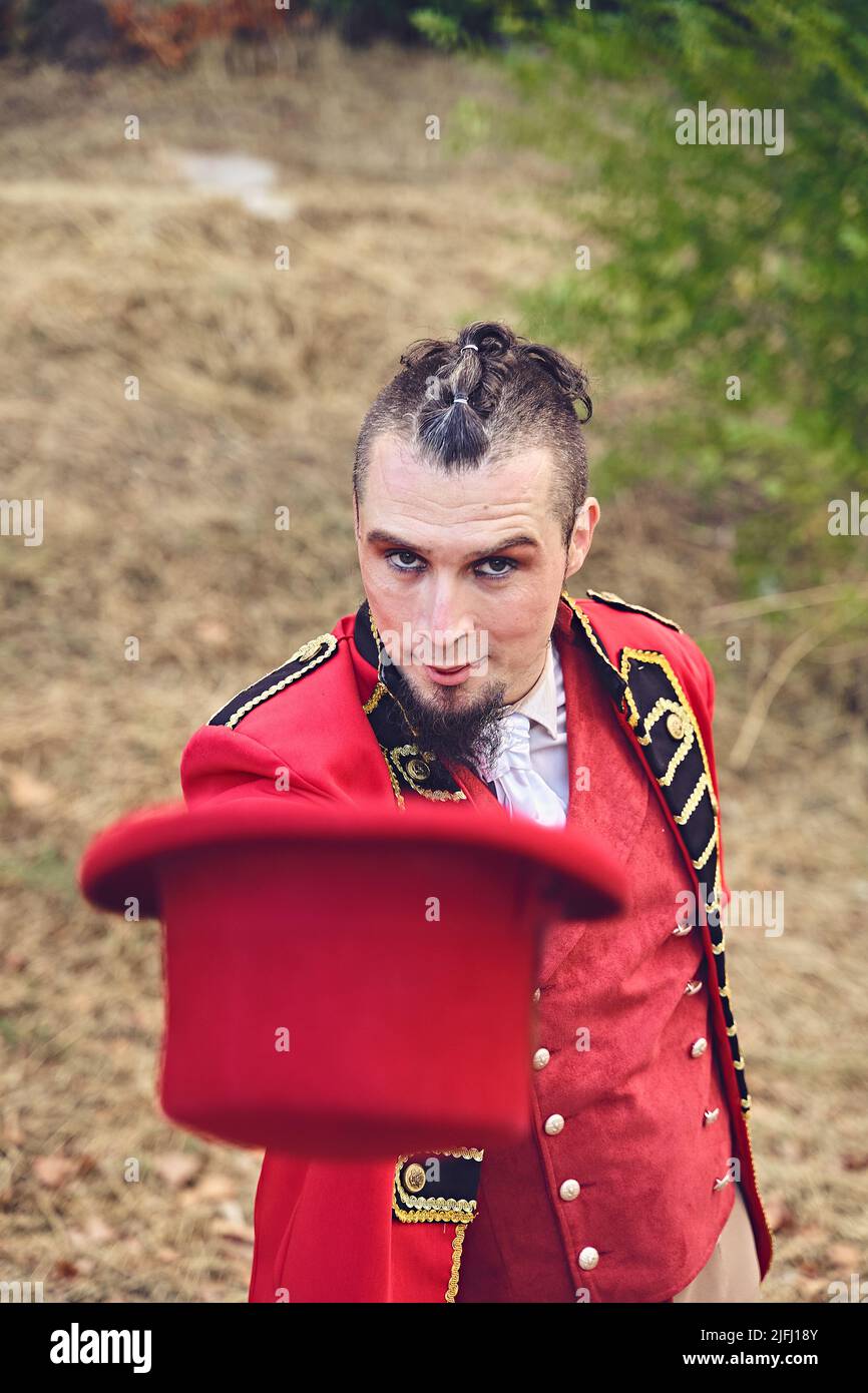 Hoher Winkel des Mannes in schickes rotes Anzug zeigt Hut und Blick auf die Kamera während der Performance im Park Stockfoto