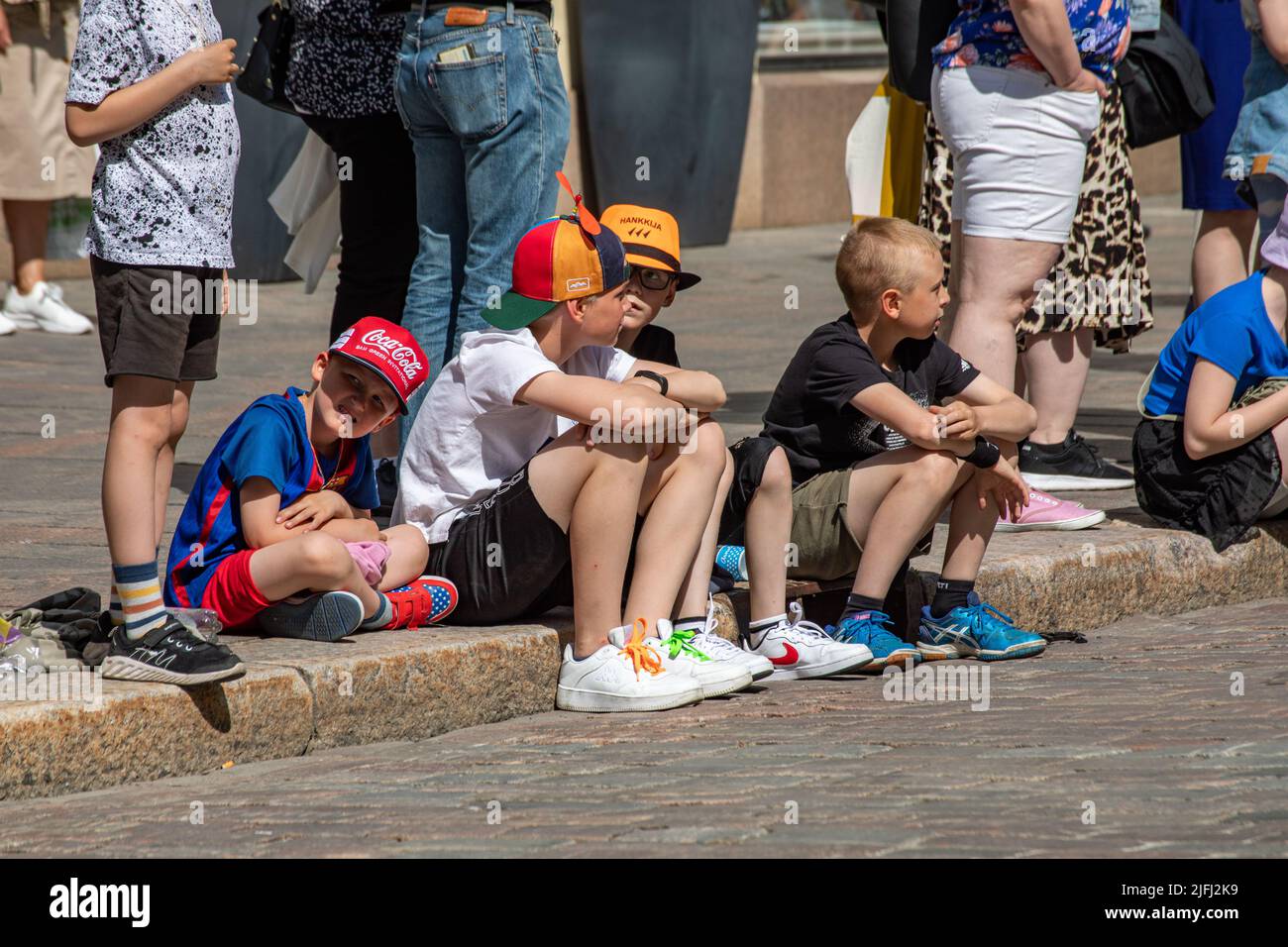 Junge Jungen sitzen auf einem Randstein und warten auf die Samba-Karnevalsparade in Pohjoisesplanadi, Helsinki, Finnland Stockfoto