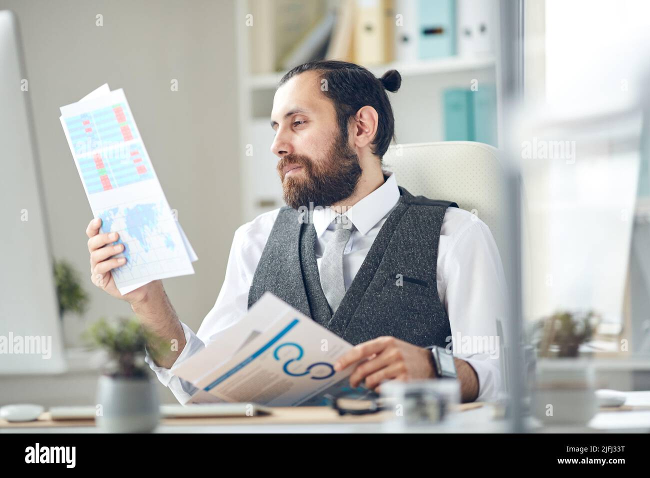 Content Zufrieden Business Analyst mit Bart sitzen am Tisch und betrachten Papiere während der Arbeit mit Analytics im Büro Stockfoto