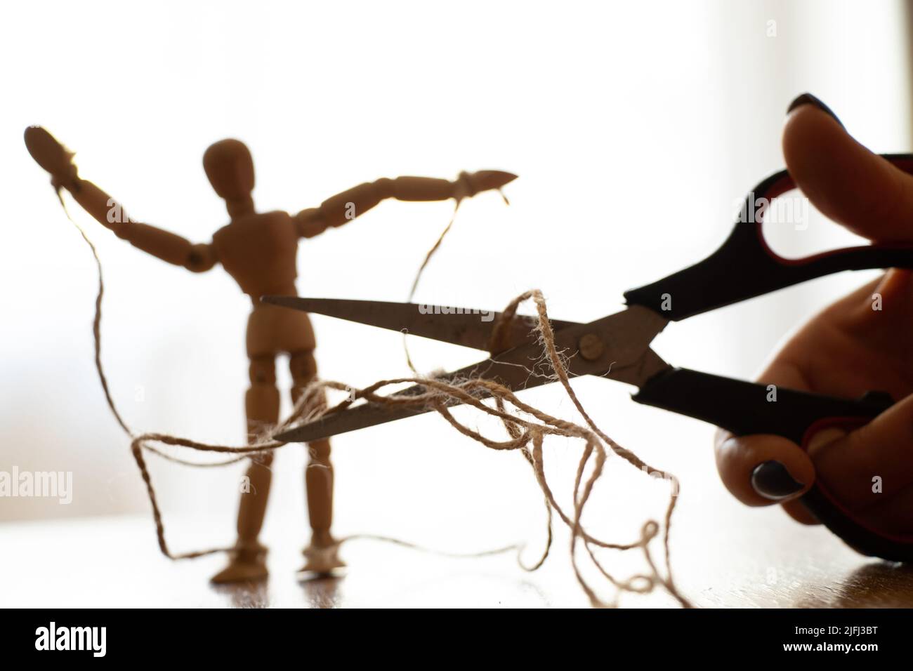 Holzpuppe mit Seilen an den Puppenspieler gebunden und Schere schneiden das Seil, Manipulation von Menschen und Freiheit, Kraft und Freiheit über Macht Stockfoto